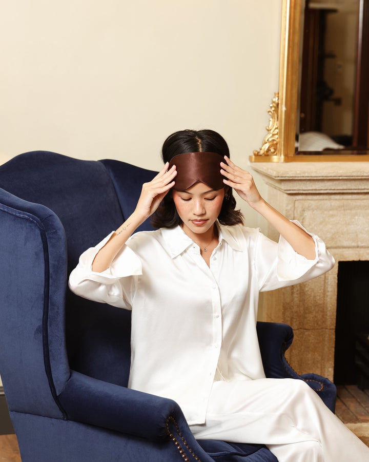 Espresso silk eye mask putting on pearl white pyjamas armchair