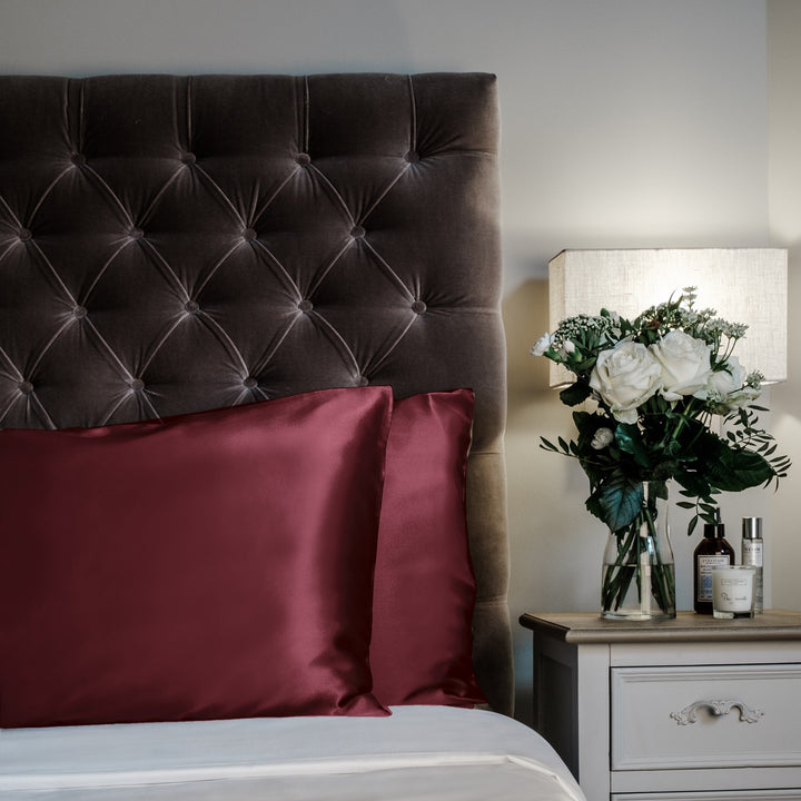 Maroon limited edition mulberry silk pillowcases, 22 momme 100% silk, on a velvet headboard | The Silk Collection