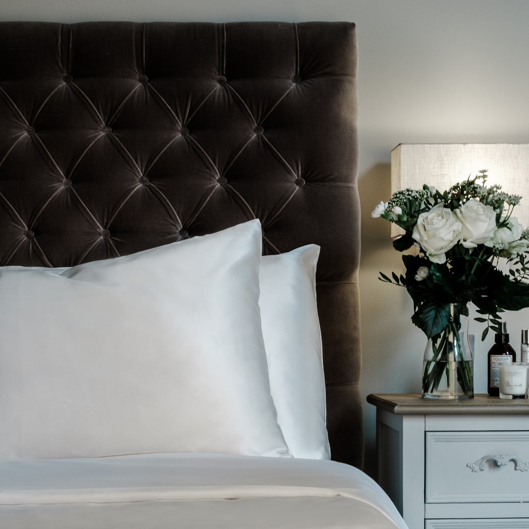 Pearl White mulberry silk pillowcases for hair and skin, 22 momme 100% silk, on a velvet headboard | The Silk Collection