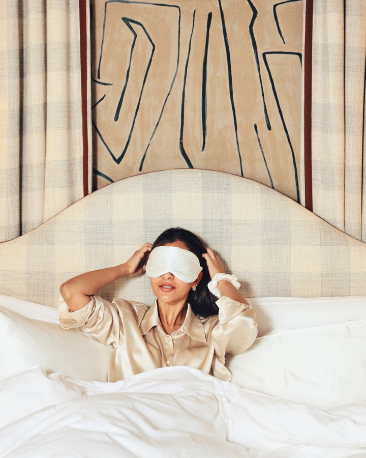 Pearl white silk eye mask over eyes arms up in bed